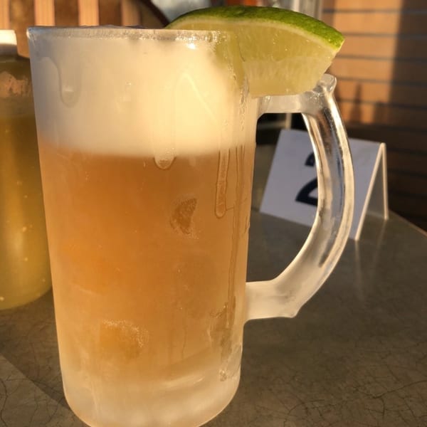 A frosty mug of Mami's Mexican Grill beer with a lime wedge on a sunny patio table.