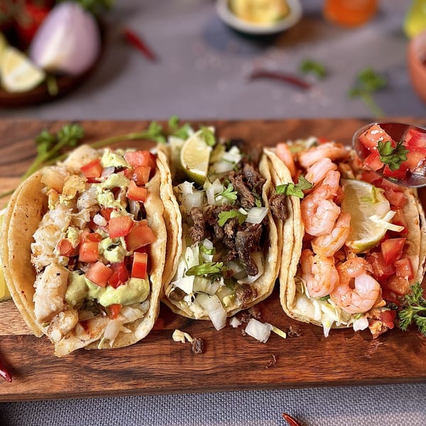 Three Mami's Mexican Grill tacos on a wooden board: fish, carne asada, and shrimp.
