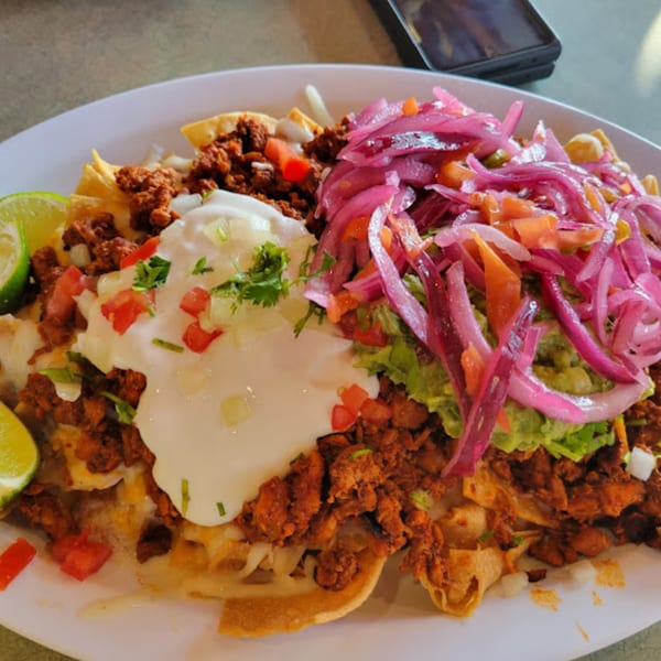 Mami's Mexican Grill nachos with chorizo, sour cream, guacamole, pickled red onions, and lime wedges.