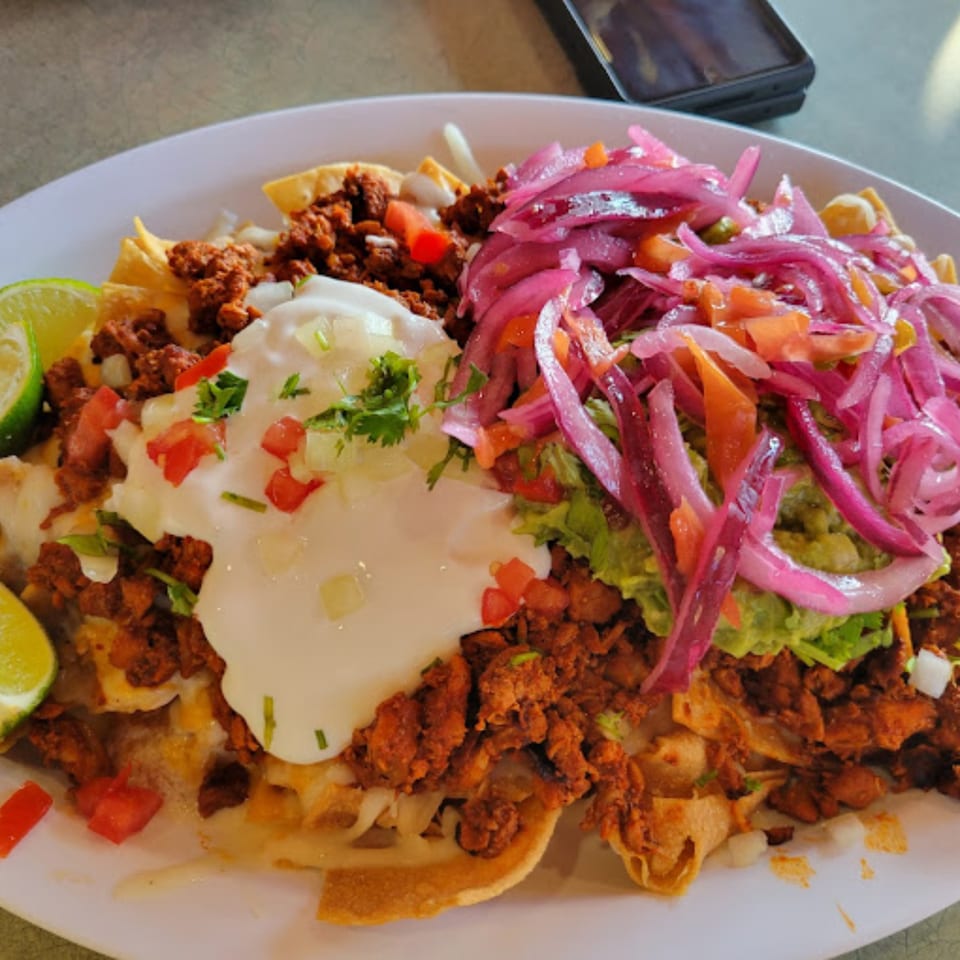 Mami's Mexican Grill nachos with chorizo, sour cream, guacamole, pickled red onions, and lime wedges.