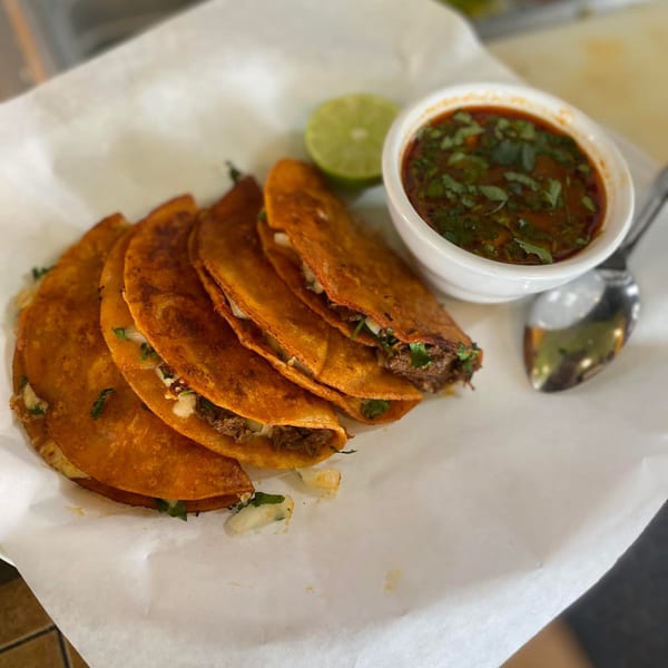 Five Mami's Mexican Grill birria tacos with a side of consommé and a lime wedge.