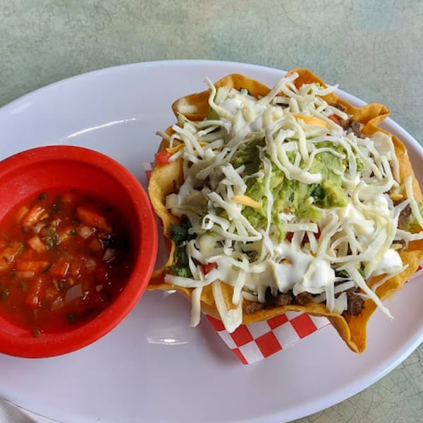 Mami's Mexican Grill taco salad with guacamole, cheese, and salsa on a white plate.